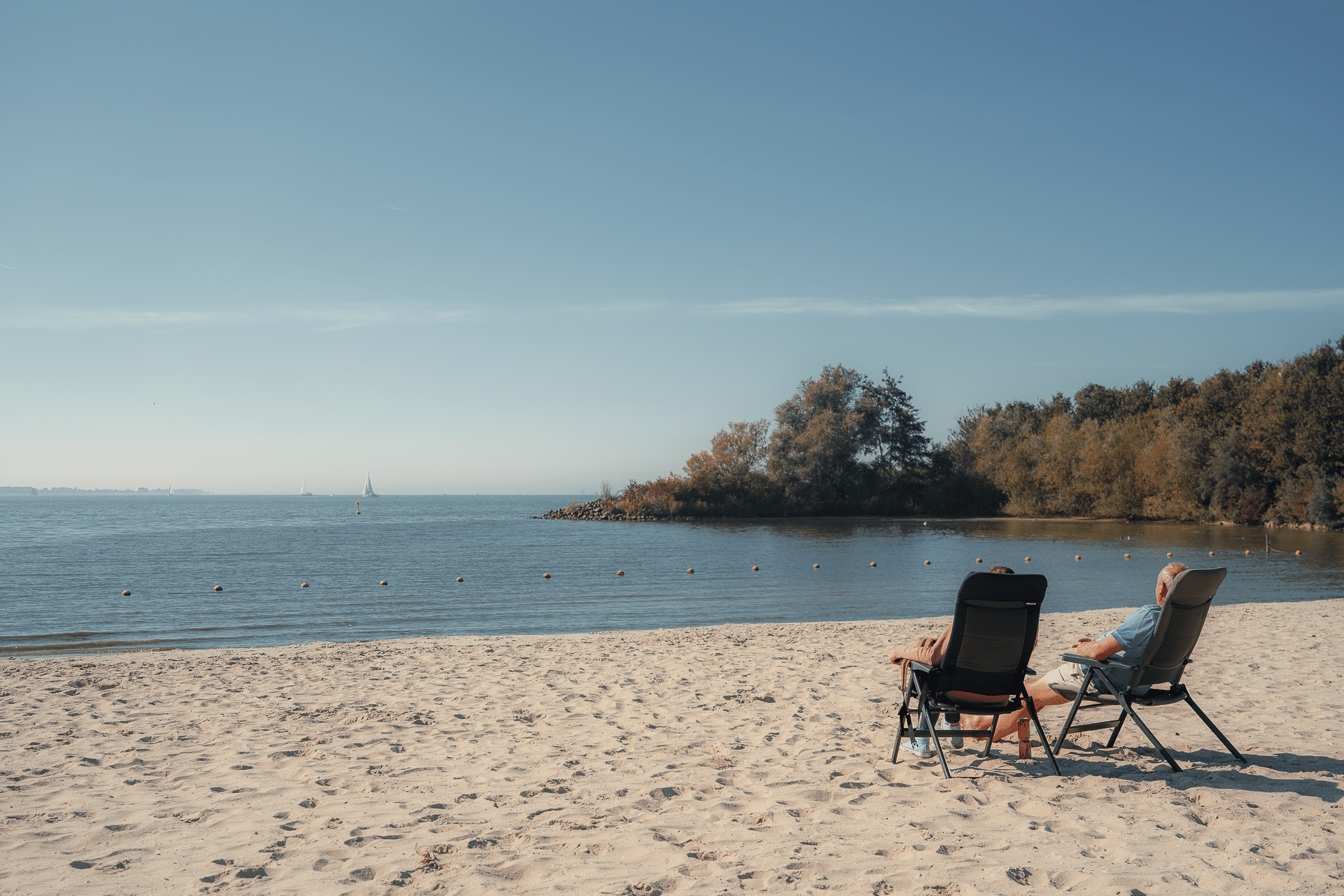 twee mensen zitten op stoelen op het strand, aan het water